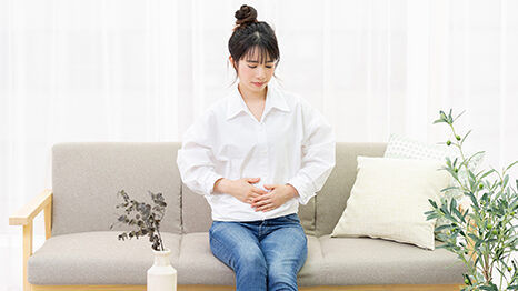 窓際のソファに座ってお腹を手で抑える若い女性